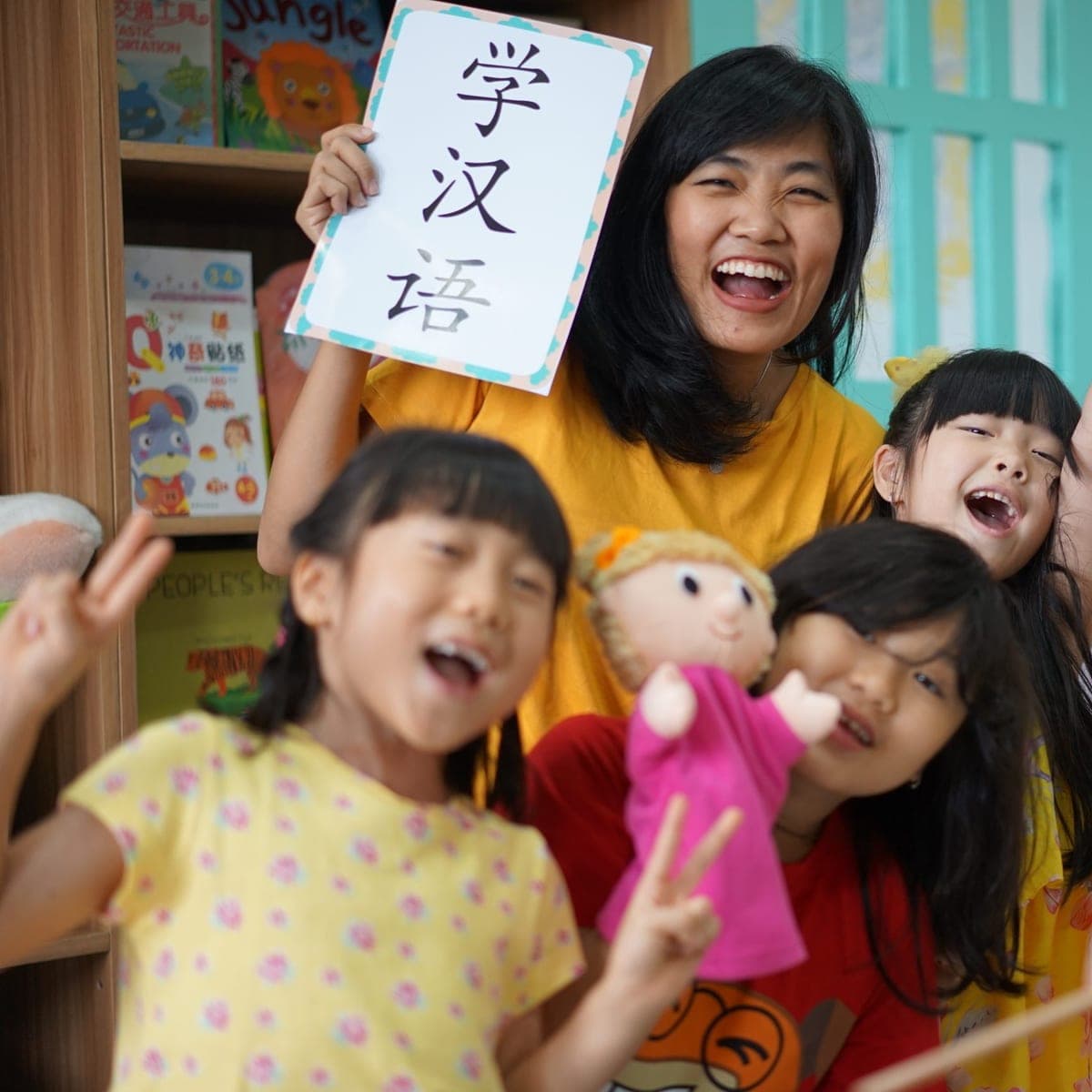 Guru Kiddles mengangkat papan bertuliskan 学汉语 bersama murid-murid yang bersorak